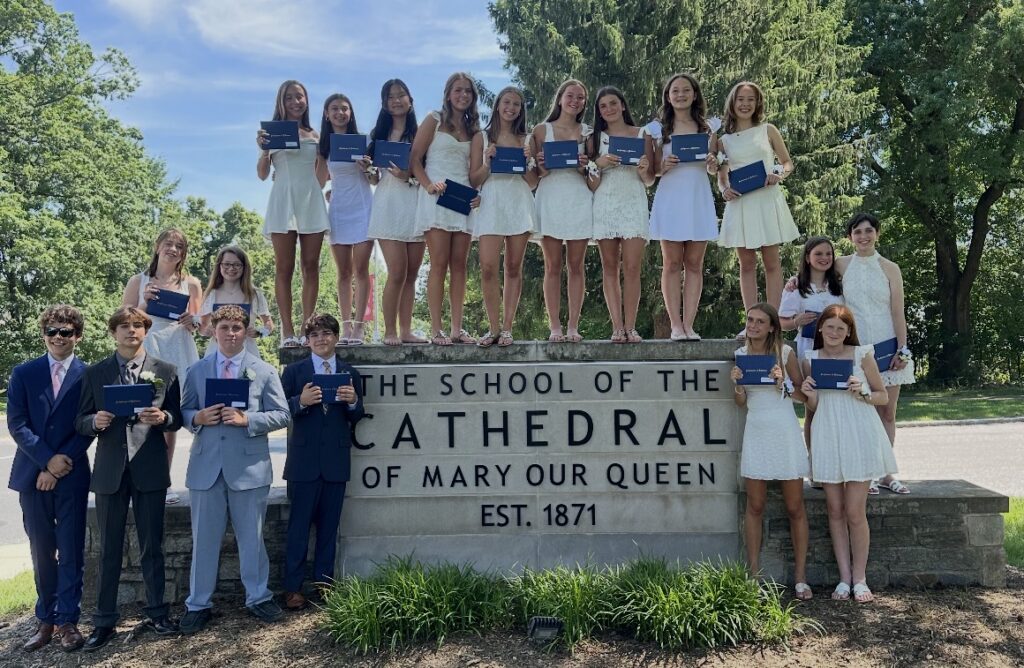 8th grade graduates in front of The School of the Cathedral of Mary Our Queen sign